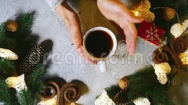 在圣诞装饰的<strong>桌子上</strong>放一杯热红茶或咖啡。 女孩的手慢慢地<strong>拿起</strong>它。 好主意继续